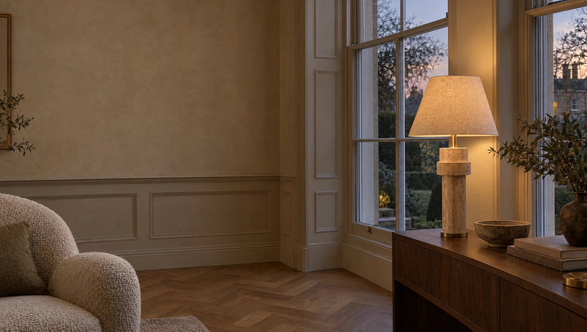 British Georgian living room at dusk with a sculptural travertine and brushed brass table lamp glowing warmly on a walnut console